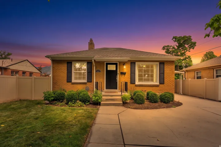 Brick exterior with a gabled roof, a concrete driveway, and a manicured front lawn, featuring a stone walkway