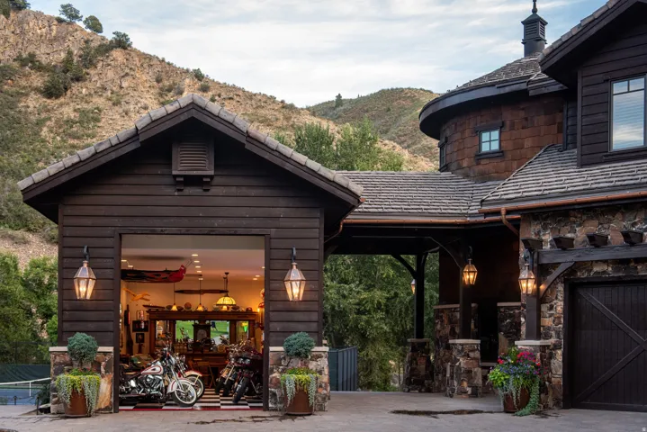 Wood-sided garage with exterior lanterns, natural stone accents, and an attached architectural element featuring a cupola and circular design