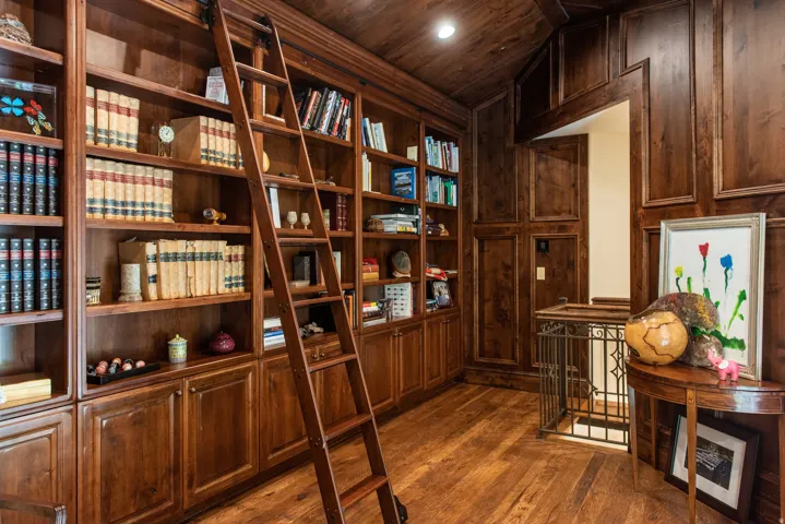 Built-in wood-finish bookcases, rolling ladder, wood-finish flooring, wood-paneled walls, and wrought iron railing