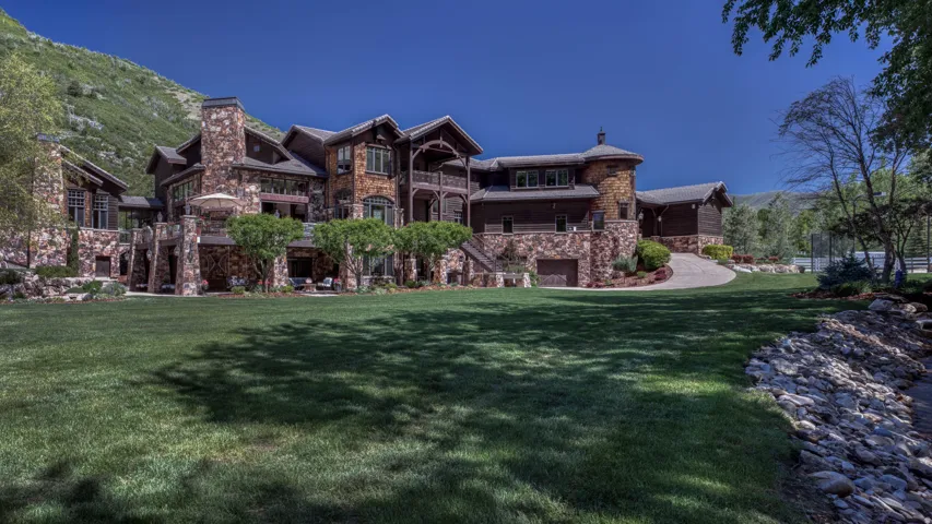 Stone and timber-clad residence featuring multiple balconies, a lower-level patio, an attached garage, and a long paved driveway