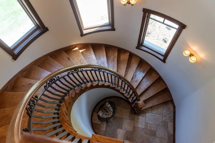 Curved wood staircase with wrought iron railing, arched windows, and wall-mounted sconces