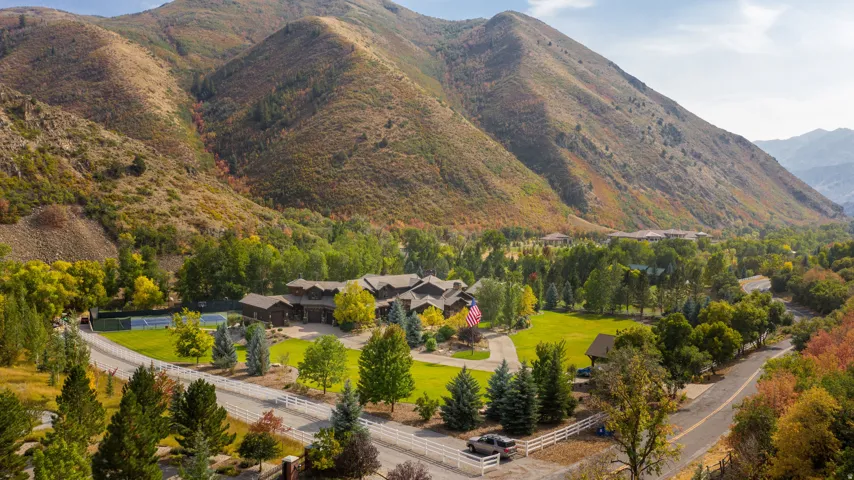 Extensive property with a natural mountain backdrop, featuring a large residence with multiple gables, a tennis court, and manicured lawns