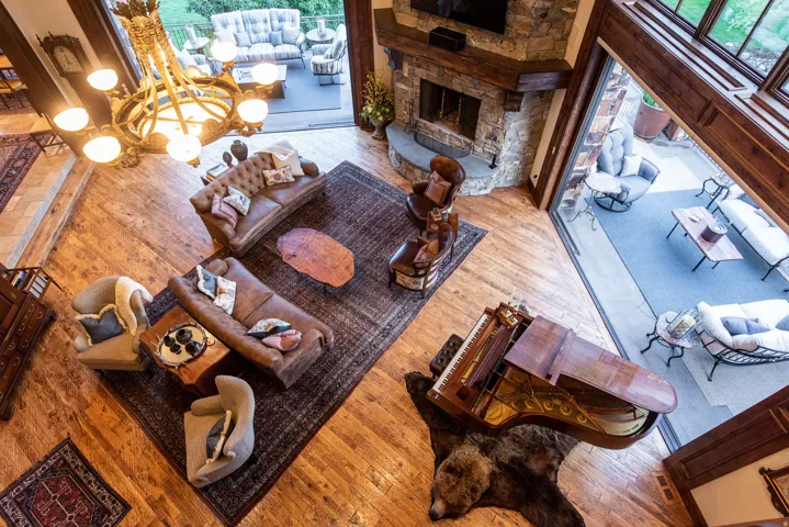 Spacious living area featuring wood-finish flooring, a stone fireplace, exposed wood beams, and a large multi-pane window wall
