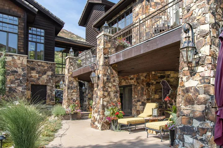 Stone and wood-sided exterior with a balcony, an outdoor patio, and built-in architectural lighting