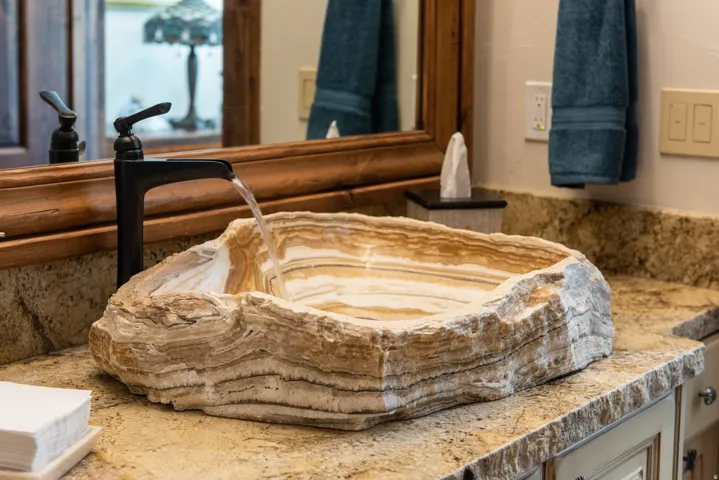 Natural stone vessel sink with a black waterfall faucet