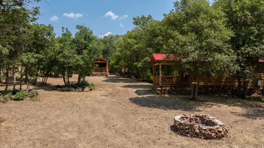 Multiple log cabin structures, covered porches with wood railings, red metal roofs, and a stone fire pit