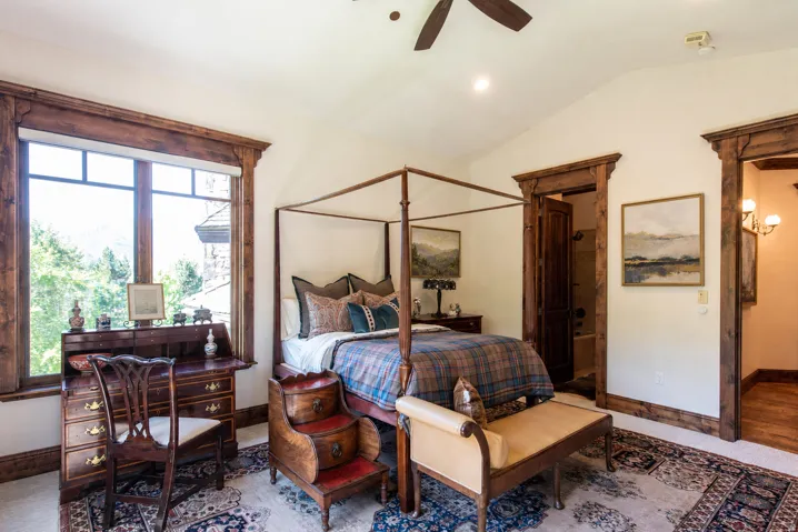 Vaulted ceiling with a ceiling fan, extensive wood trim, large window with ample natural light, and a dedicated doorway to a full bathroom