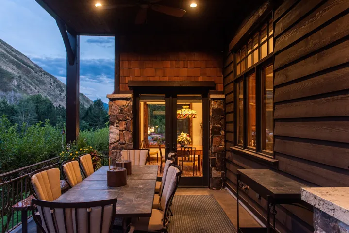Covered outdoor living space featuring stone columns, wood siding, and an ornate metal railing