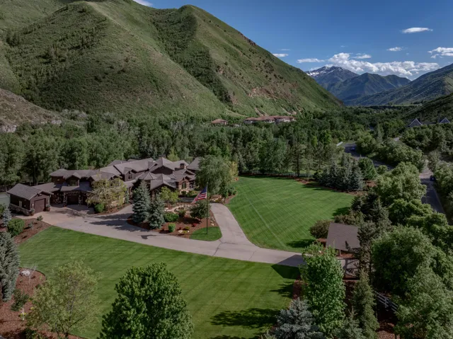Expansive estate featuring a large, multi-gabled residence with a dark-toned exterior and numerous surrounding trees
