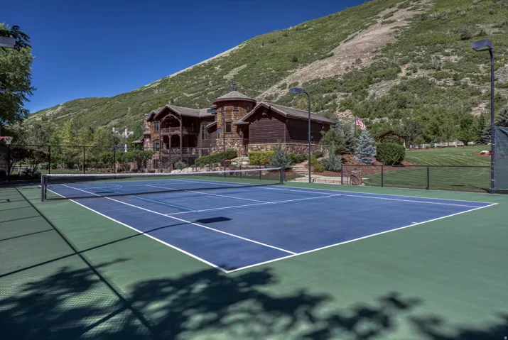 Multi-sport court featuring a tennis net, basketball hoop, and perimeter fencing