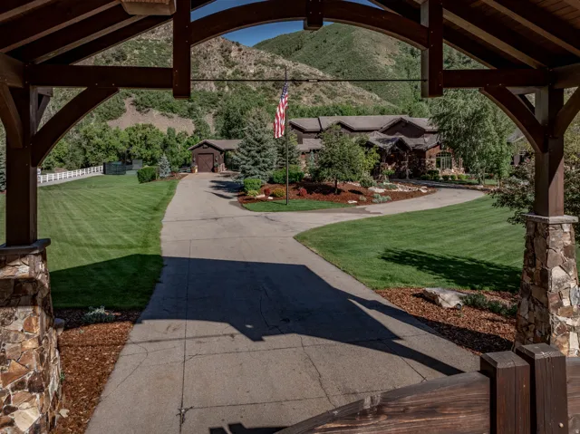 Arched timber frame entry with stone-clad columns, opening to a paved drive and extensive lawn areas