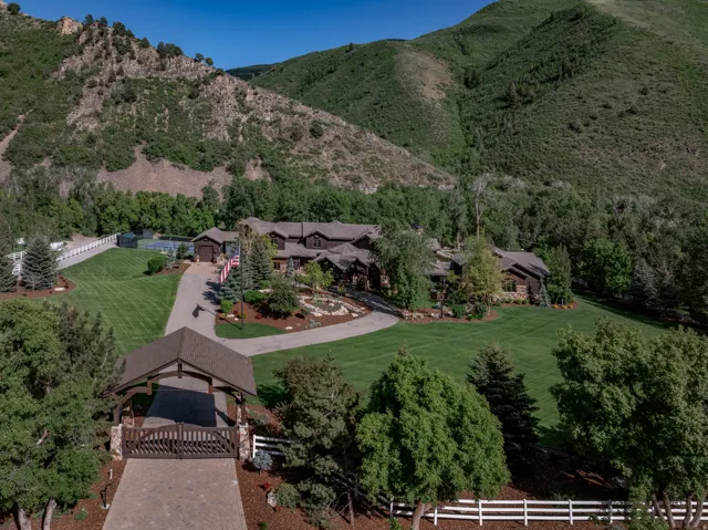 Extensive property featuring a large residence, tennis court, and gated entry, all surrounded by mature landscaping and mountain scenery