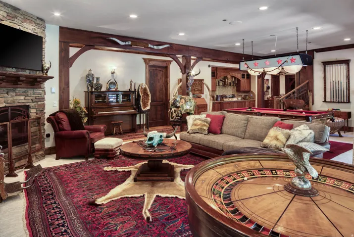 Spacious entertainment area featuring a stone-clad fireplace, exposed wood beams, and recessed lighting