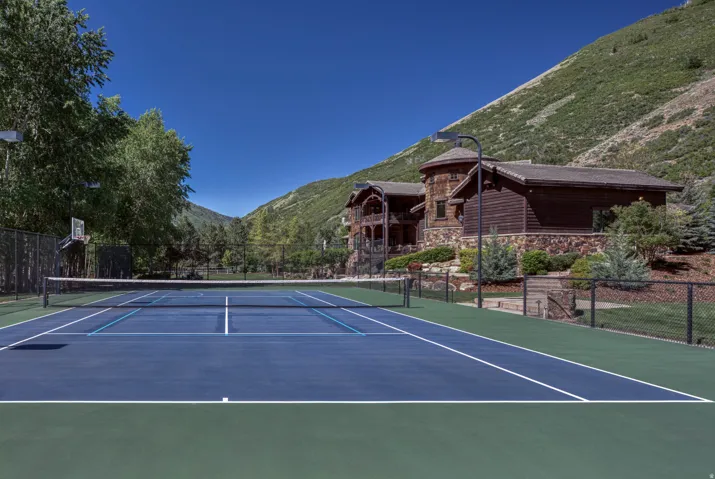 Outdoor tennis court featuring a blue playing surface with white lines, green perimeter, and a net