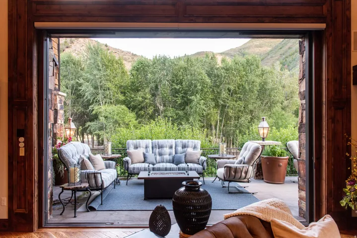 Expansive outdoor patio with stone columns, wood-framed sliding glass doors, and a natural mountain backdrop