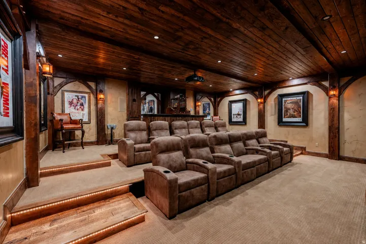 Luxury home theater featuring tiered seating with power-recline leather upholstery, wood-finish ceiling with recessed lighting, arched architectural detailing, framed artwork displays, and premium carpeting throughout