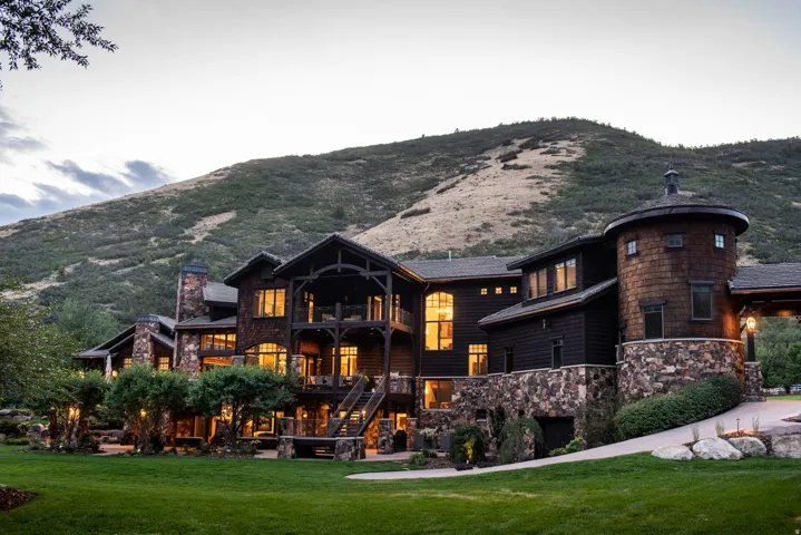 Multi-level exterior featuring natural stone and dark wood siding, a prominent round turret with shingle siding, multiple balconies, and a manicured lawn
