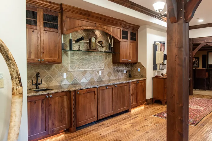 Built-in wet bar with wood cabinetry, granite countertop, and tiled backsplash