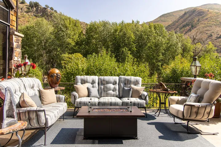 Expansive outdoor patio with a built-in fire pit, stone exterior wall, and metal railing