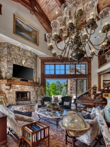 Great room featuring a vaulted wood-plank ceiling with exposed timber beams, a stone fireplace, and expansive windows