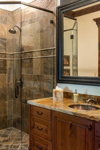 Glass-enclosed shower with tiled walls and floor, wood-finish vanity with stone countertop, and an integrated basin