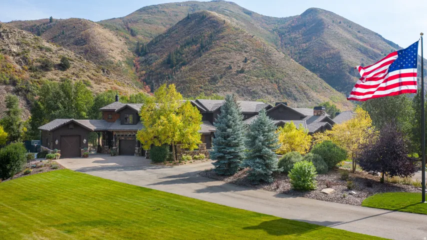 Property featuring a multi-gable roofline, stone accents, attached garage, and a paved driveway, all set against a mountainous backdrop