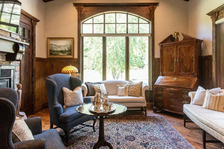 Arch-top window with grid detailing, wood-finish flooring, half-wall wood paneling, wood beam ceiling, and a stone-clad fireplace