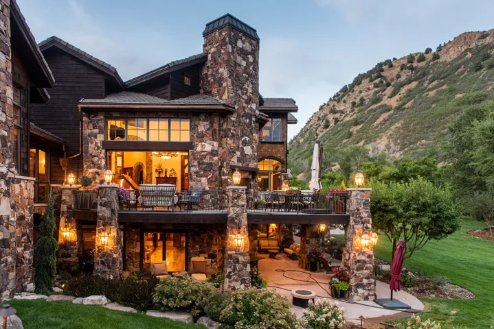 Stunning stone exterior featuring a prominent chimney and multi-level architecture overlooking manicured grounds and mountain backdrop