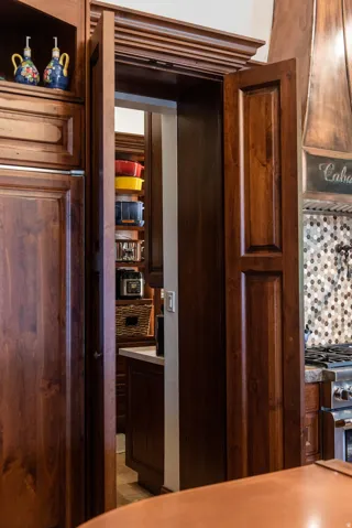 Rich wood-finish cabinetry with crown molding, integrated refrigerator panel, and a decorative range hood
