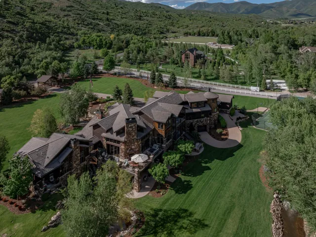 Expansive stone and timber residence featuring multiple gabled roofs, a circular driveway, and a private tennis court