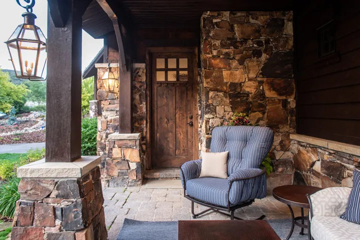 Covered front porch featuring natural stone accents, substantial wood columns, a paneled wood entry door with glass inserts, and paver flooring