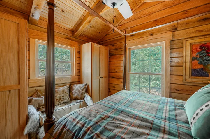Wood-paneled walls and ceiling with exposed beams, built-in window bench, two double-hung windows, and a ceiling fan