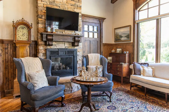 Stone fireplace with wood mantel, hardwood flooring, large picture window, wood paneling, and a dark wood paneled door