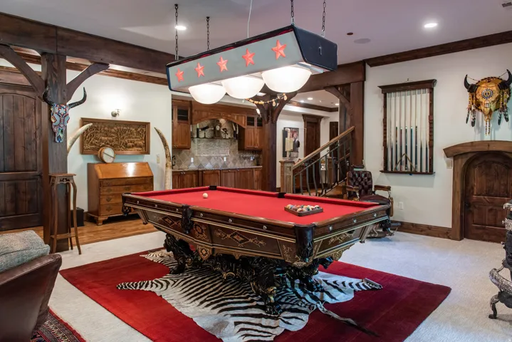 Recreation room featuring exposed wood beams, a built-in wet bar, wood-paneled archways, a metal railing staircase, and a built-in cue rack