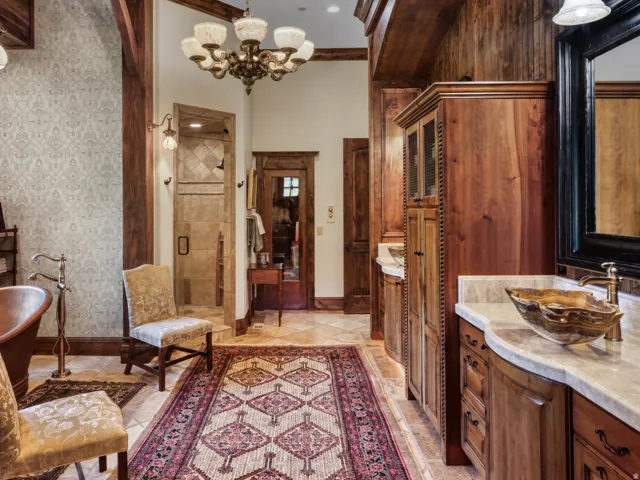 Wood-paneled walls and ceiling, dual vanity with vessel sinks, walk-in shower with tiled surround, freestanding soaking tub with floor-mounted faucet, and a decorative chandelier