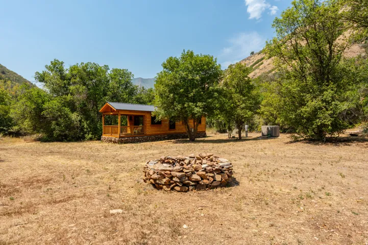 Wood-sided cabin featuring a covered porch with wood railings, a metal roof, and a stone-built fire pit