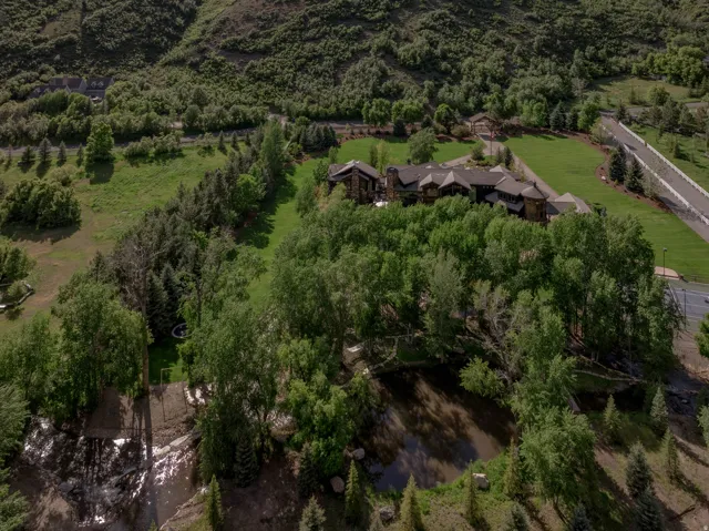 Expansive estate featuring a large, multi-building residence, mature trees, a private pond, extensive manicured lawn areas, and a paved driveway with a gated entrance