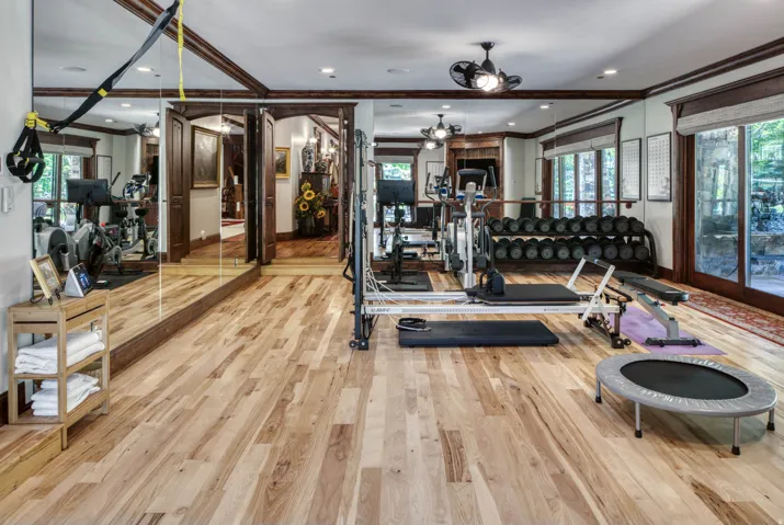Dedicated fitness area featuring wood-finish flooring, extensive wall-mounted mirrors, recessed lighting, and dark wood trim details