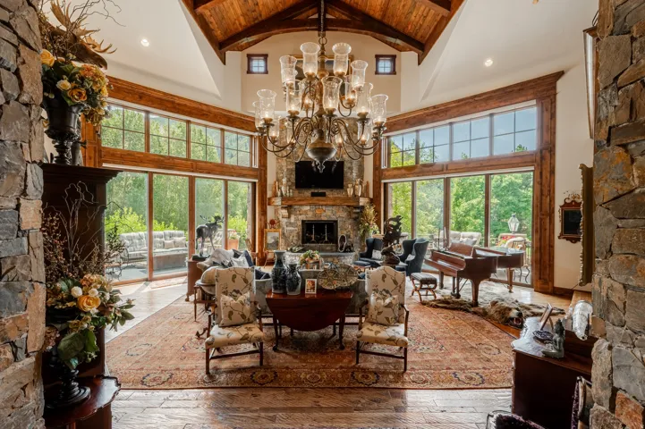 Vaulted wood-finish ceilings with exposed beams, stone-clad walls, expansive floor-to-ceiling windows, and a built-in stone fireplace
