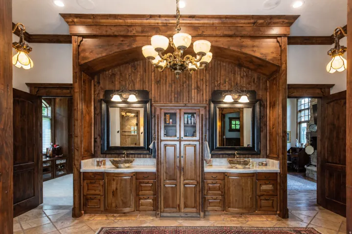 Dual vanity with vessel sinks, wood cabinetry, stone countertops, wood paneling, and a chandelier