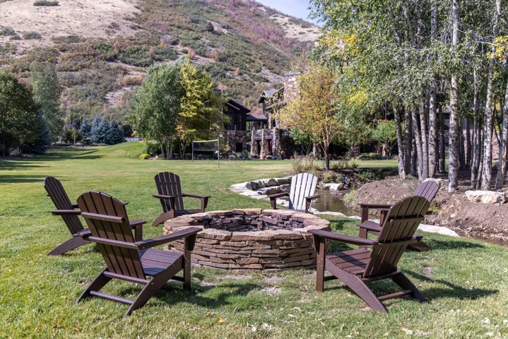 Expansive lawn featuring a stone-clad fire pit, surrounded by Adirondack chairs