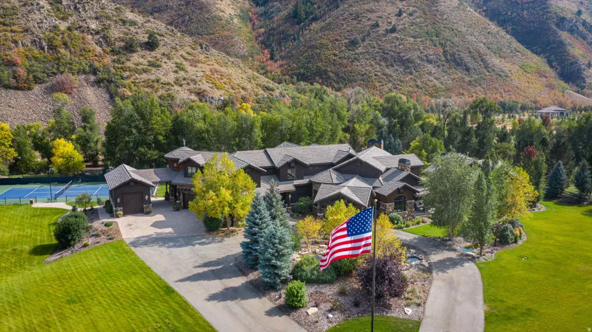 Extensive property featuring a multi-gabled roofline, a private tennis court, mature landscaping, and a paved driveway