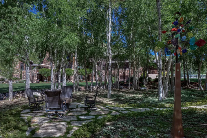 Lush outdoor space featuring a flagstone patio, mature birch trees, and a stone facade residence in the background