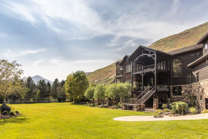 Expansive grassy lawn with a curved stone patio, multi-level covered balconies, and a stone and wood-clad exterior