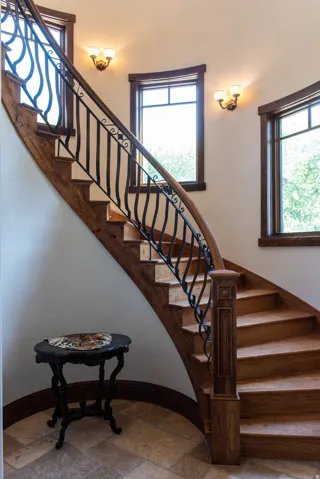 Curved wood staircase featuring a decorative wrought iron railing and carved newel post