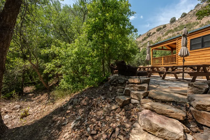 Log cabin structure with a covered porch featuring wood railings, a stone patio, and natural stone steps