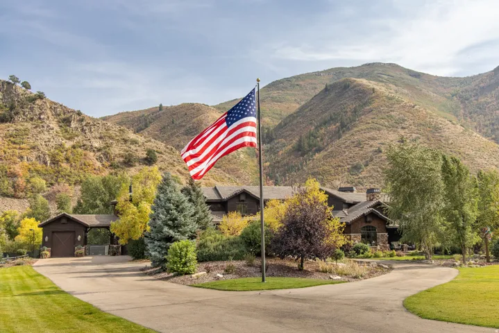 Mountain-side residence with a circular driveway, mature landscaping, and an attached garage with a covered walkway