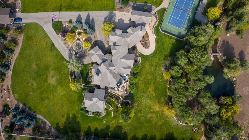 Expansive property featuring a multi-wing residence, private tennis court, winding driveway, mature landscaping, and an ornamental pond with bridge
