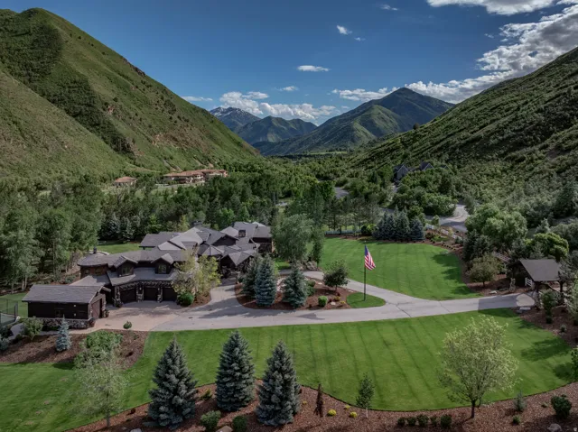 Expansive estate featuring a large main residence with multiple gables, extensive paved driveway, lush green lawns, mature evergreen trees, and a tennis court
