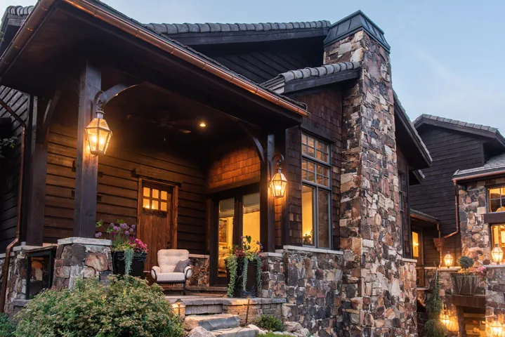 Stone and wood-sided exterior with a covered porch, multiple fixed windows, and a prominent stone chimney